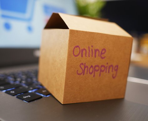 En öppnad låda i pappkartong ovanpå en bärbar dator. På lådan står texten "online shopping" handskriven.